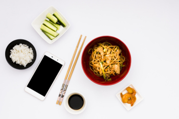 Mobile phone with tasty asian food over white surface