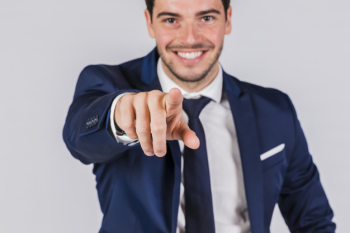 Happy young businessman pointing his finger at camera on grey background Free Photo