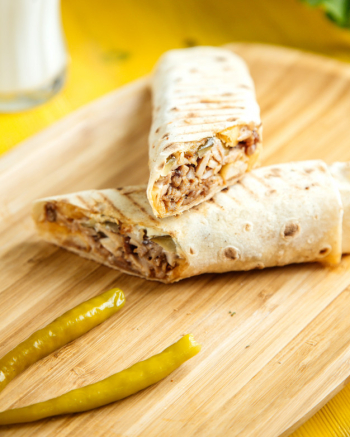 Close up view of chicken doner wrapped in lavash with pickled green pepper on wooden platter Free Photo