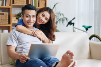 Asian man relaxing on couch with laptop at home and happy woman hugging him Free Photo