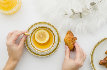 Close-up of a person's hand having croissant with lemon tea on white background Free Photo