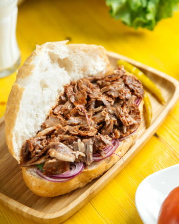 Side view of beef doner in bread with pickled green pepper on wooden platter Free Photo