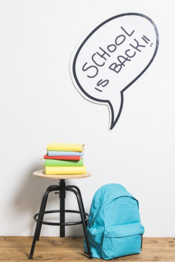 Stack of books on stool chair and school bag talking by speech bubble Free Photo