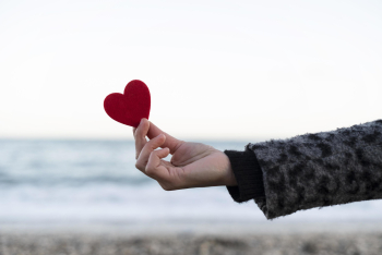 Woman&#39;s hand holding a red heart on the seashore. concept of valentines day Free Photo