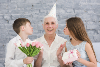 Joyful elder woman sitting in between her grandchildren with flowers bouquet and gift box Free Photo