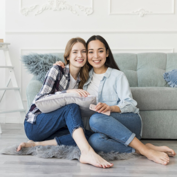 Ladies sitting embracing on floor barefoot with pillow and mobile phone Free Photo