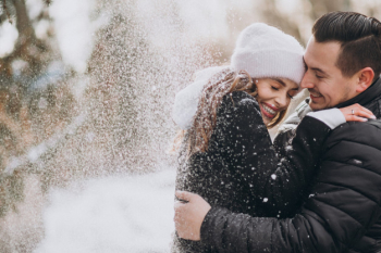Young couple in winter under the snow falling from the tree Free Photo