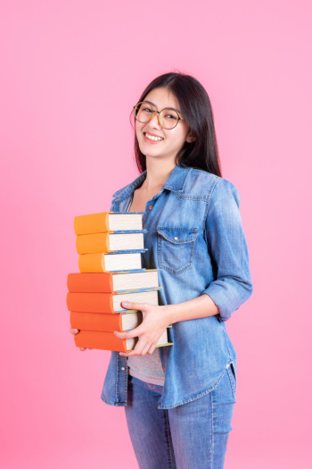 Portrait teenage pretty girl holding stack of books and smiley on pink, education teenge concept Free Photo