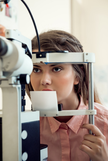 Horizontal portrait of focused european woman testing sight while looking through microbioscope, sitting in specialist office, wanting to pick appropriate glasses to see better Free Photo