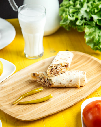 Side view of chicken doner wrapped in lavash with pickled green pepper on wooden platter Free Photo