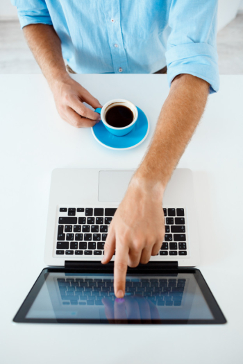 Close up picture of young businessman's hands sitting at table pointing on laptop screen holding coffee cup. white modern office interior Free Photo
