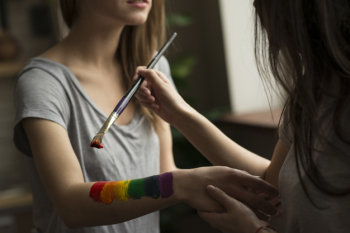 Young woman painting the rainbow flag over her girlfriend's hand Free Photo