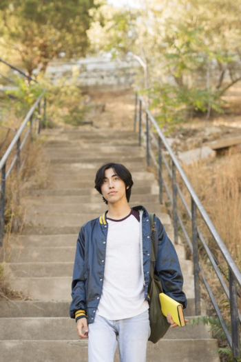 Asian teenager walking down stairs with book in hand Free Photo