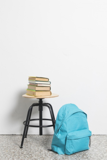 Stack of books on stool chair with blue schoolbag on floor Free Photo