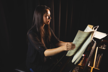 Female student looking at sheet music while playing a piano Free Photo