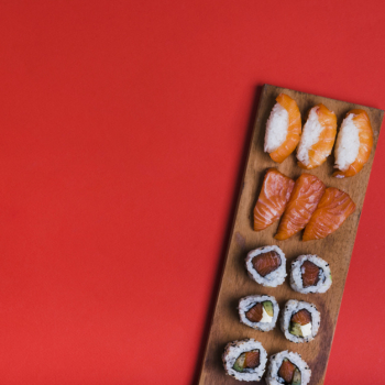 Assortment of sushi on wooden tray against red backdrop with copy space for writing the text Free Photo
