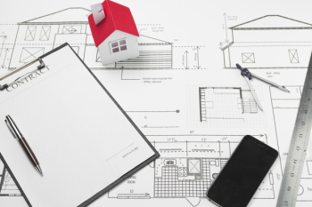 Cellphone and clipboard with small house model on blueprint Free Photo