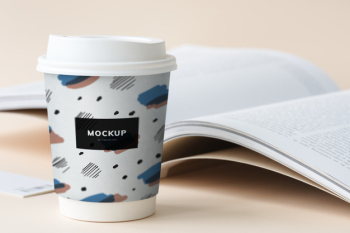 Takeaway coffee cup mockup on a table with an open book Free Psd