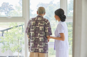 a nurse and a senior man are standing and looking outside from glass window