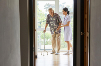 a nurse is helping a senior man walking indoors