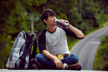 a handsome guy is sitting, drinking and relaxing on the road in forest
