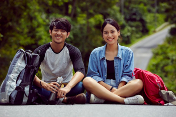 a couple of asian young travellers are smiling and sitting together