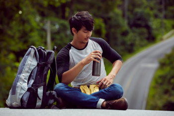 a handsome man is holding a flask of water and sitting on a road in forest