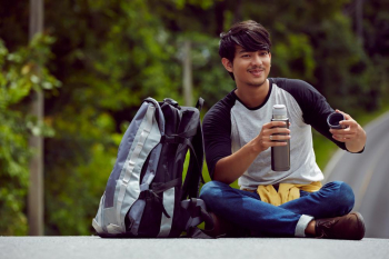 a handsome man with smile is holding a flask of water and relaxing on a road