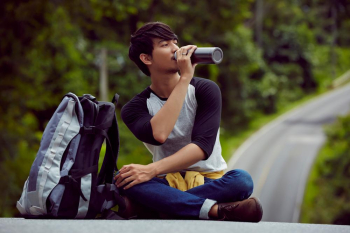 a handsome guy is sitting to relax and drinking water in forest