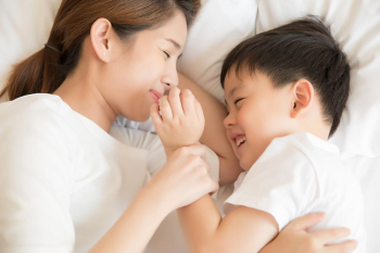 A young mother and her baby is laughing together while lying on bed