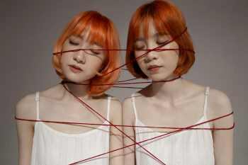 Two young girls who look alike are standing and tied together by a red string