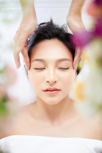 A young woman with happy face is lying relax, enjoying head massage inside a spa 