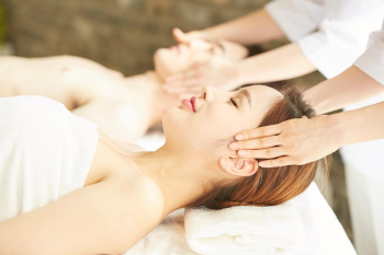 Smiling young woman and young man are lying on their back and enjoying head massage at a beauty salon