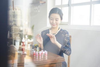 A beautiful young woman in a stylist dress is painting her fingernails at the make up table full of cosmetic products