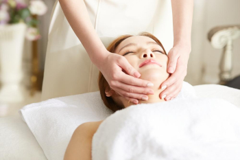 A young woman  closes her eyes enjoying face massage inside a spa