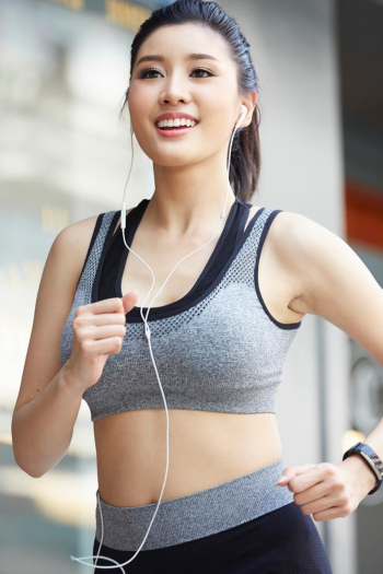 A young woman in sport-wear is running while listening to music with smiling face