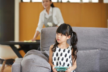 A photo of cute little girl sitting on the sofa at home.