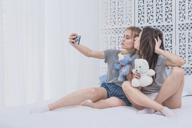 pouting,indoors,softness,taking,fashionable,bonding,homosexual,posing,togetherness,lesbian,casual,girlfriend,self,two,stylish,pretty,shorts,passion,adult,holding,joy,relationship,soft,cell,lifestyle,sitting,beautiful,young,cellphone,together,female,friendship,selfie,toy,fun,bed,curtain,toys,friends,smartphone,couple,women,mobile,beauty,phone,camera,woman,technology,love,people