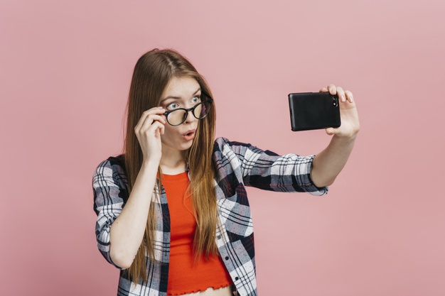 medium shot,gesturing,front view,expressive,taking,medium,appearance,casual,front,feeling,surprised,horizontal,shot,adult,look,facial,gesture,portrait,expression,view,emotion,young,youth,selfie,studio,model,person,pink background,glasses,human,colorful,wall,pink,phone,woman,background